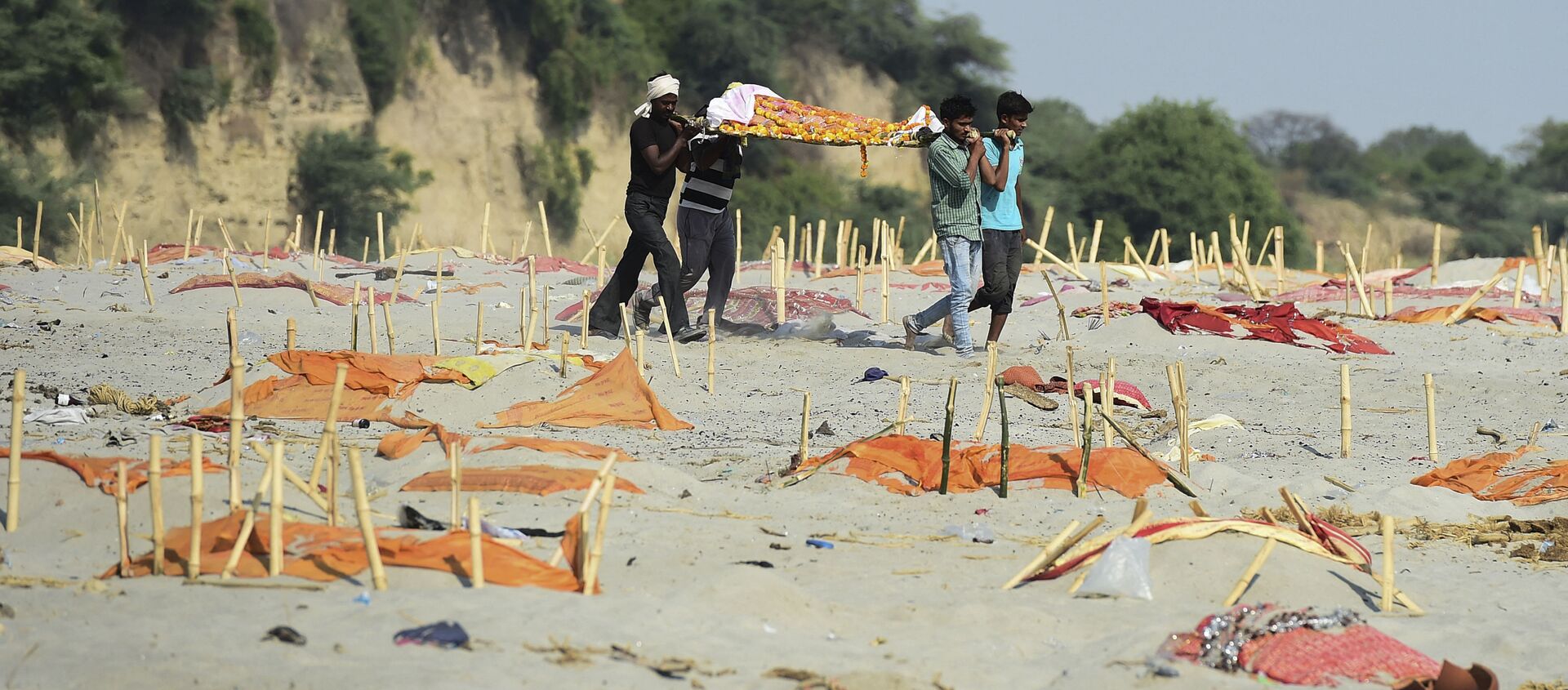 Hindistan'da sularından yüzlerce Kovid-19 kurbanının cansız bedenlerinin toplandığı Ganj Nehri'nin kıyılarındaki kumlarda üstünkörü kazılmış ve üzeri turuncu renkli kumaşlarla örtülmüş mezarlar da bulundu.  - Sputnik Türkiye, 1920, 16.05.2021