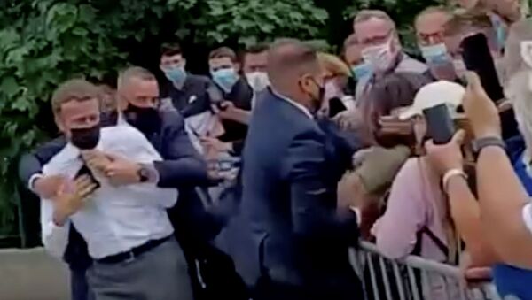 Cumhurbaşkanı Emmanuel Macron, Fransa'nın  Drome bölgesinde yurttaşlarla el sıkışırken tokatlanmasının ardından korumaları tarafından uzaklaştırılırken - Sputnik Türkiye