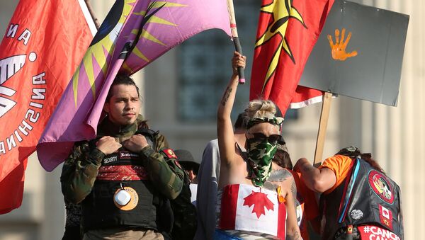1 Temmuz Kanada Günü'nün yerli çocuk mezarlarının gölgesinde kutlanmasında ısrar edilince, Winnipeg kentindeki Manitoba eyaleti parlamento binası önünde Kraliçe Victoria heykelini yıkıp kaidesine çıkan protestocular - Sputnik Türkiye
