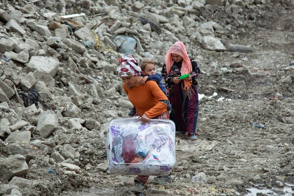 Bir kadın, enkazın ve çamurun içinde sırtındaki çocuğu ile gelen yardımlardan aldığı bir yorganı ve birkaç çocuk elbisesini evine götürüyor.
 - Sputnik Türkiye