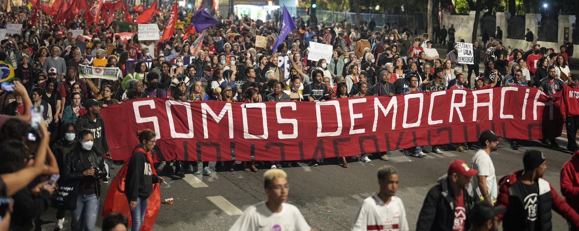 Brezilya'nın Sao Paulo şehrinde Portekizce Biz Demokrasiyiz yazılı pankart açarak yürüyen göstericiler, 8 Ocak 2023'te devlet başkanlığı, Kongre ve Yüksek Mahkeme'yi basarak darbe girişiminde bulunan önceki Devlet Başkanı Jair Bolsonaro'nun taraftarlarının yargılanıp hapse atılmasını ve demokrasinin korunmasını talep etti.  - Sputnik Türkiye, 1920, 10.01.2023