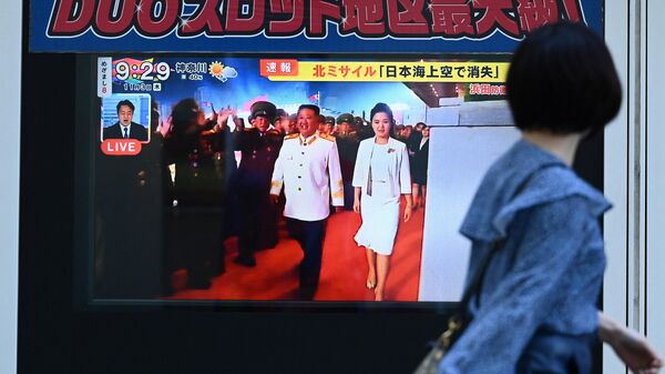 Kuzey Kore lideri Kim Jong-un ile eşi Ri Sol-ju'nun ekrandaki görüntülerine bakan Japonya'nın başkenti Tokyo'daki yayalar  - Sputnik Türkiye