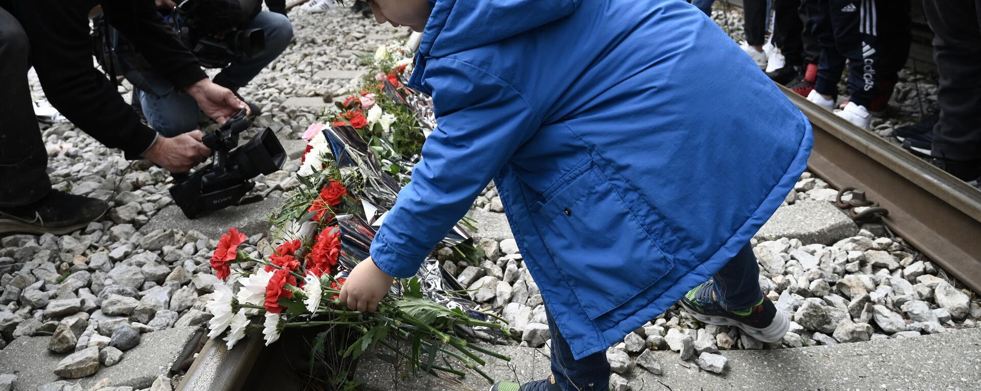 Yunanistan yurttaşları, Larisa kentinin kuzeyindeki Tempi bölgesinde yolcu treni ile yük treninin çarpıştığı kaza yerinde rayların üzerine kurbanların anısına çiçek bırakırken - Sputnik Türkiye, 1920, 07.03.2023