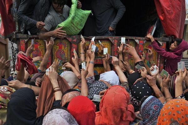 Pakistan'da hükümet, kayıtlı ihtiyaç sahiplerine Ramazan ayında tüketilmesi amacıyla un dağıttı. Fotoğrafta, kimlik kartını göstererek un yardımından yararlanmak isteyen Pakistanlı kadınlar görülüyor. - Sputnik Türkiye