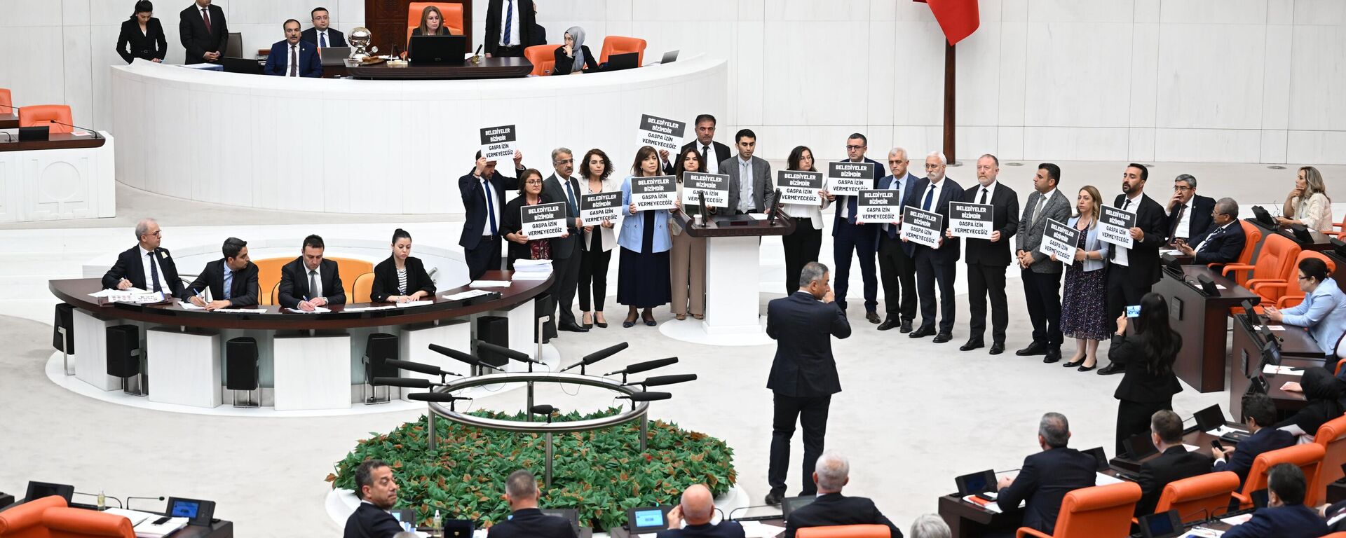 TBMM Genel Kurulunda Saadet Partisi ve İYİ Parti'nin grup önerilerinin görüşülmesinin ardından DEM Parti'nin grup önerisi üzerindeki görüşmelere geçildi. Partisinin grup önerisi üzerinde söz alan DEM Parti Hakkari Milletvekili Vezir Coşkun Parlak, Mehmet Sıddık Akış'ın Hakkari Belediye Başkanlığı görevinden alınmasını eleştirdi. Parlak'ın konuşmasının ardından DEM Parti milletvekilleri Belediyeler bizimdir, gaspa izin vermeyeceğiz yazılı dövizlerle kürsünün etrafında toplandı. - Sputnik Türkiye, 1920, 04.06.2024