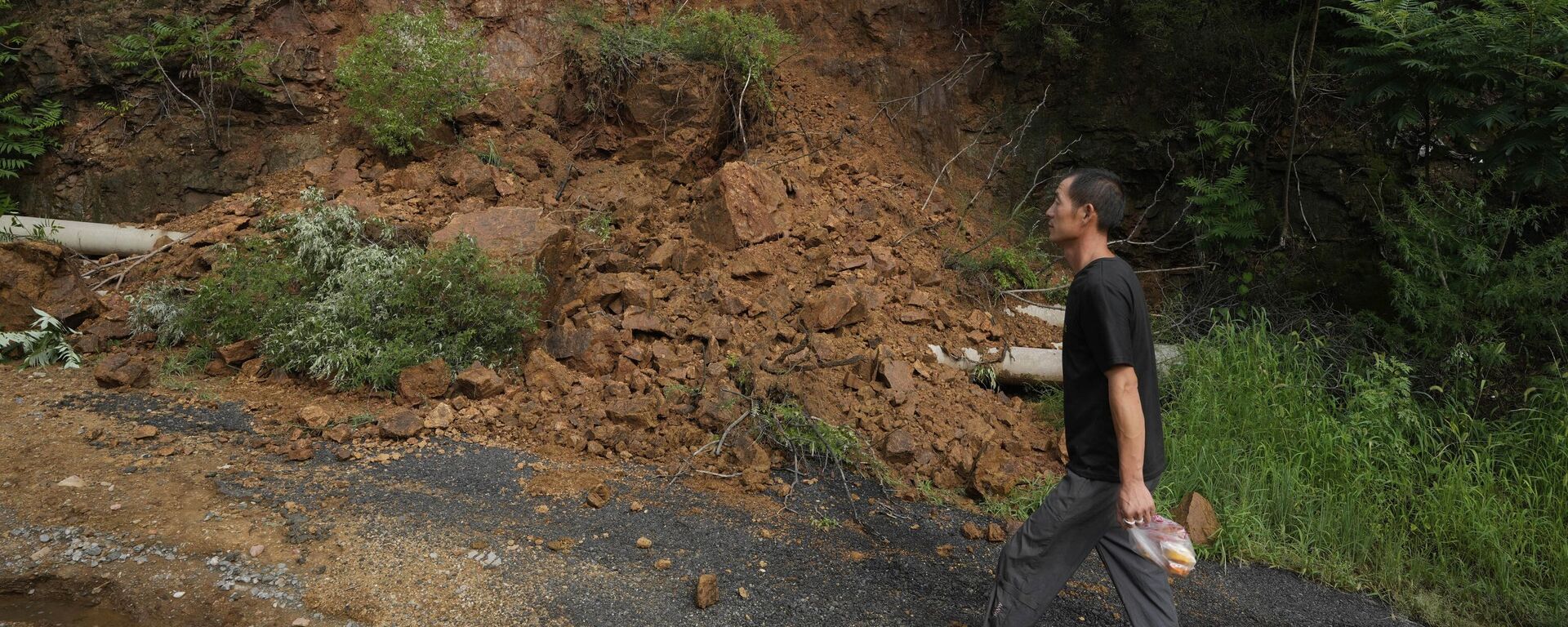 A man walks past a landslide after heavy rain in Miyun district on the outskirts of Beijing, China, Monday, July 28, 2025. - Sputnik Türkiye, 1920, 29.07.2025