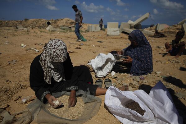 Filistinli kadınlar, havadan atıldıktan sonra parçalanarak dağılan yardım kolilerindeki pirinç, mercimek ve fasulyeleri toparlayıp temizlemeye çalışıyor. - Sputnik Türkiye