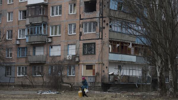 Bir kadın, Avdeyevka kentinde çatışmalar nedeniyle yıkılan çok katlı apartman binasının önünden geçiyor - Sputnik Türkiye