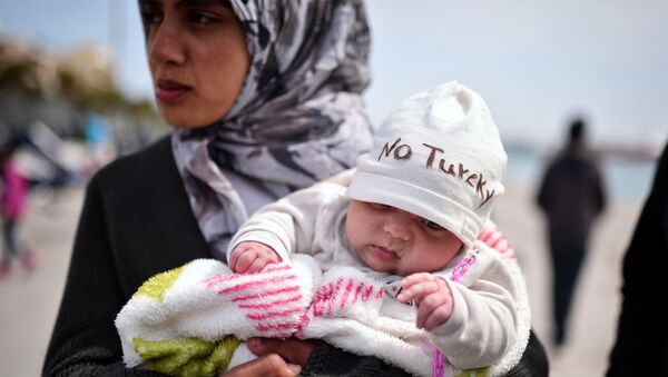 A Syrian refugee holds a two-month old baby as refugees and migrants who broke out from Chios detention camp, and camped out in the port of the city, stage a protest with their children chanting 'No Turkey' on April 3, 2016. - Sputnik Türkiye