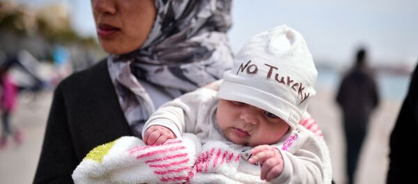 A Syrian refugee holds a two-month old baby as refugees and migrants who broke out from Chios detention camp, and camped out in the port of the city, stage a protest with their children chanting 'No Turkey' on April 3, 2016. - Sputnik Türkiye