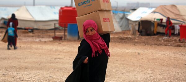 Suriyeli kadın sığınmacı Deyr Ez Zor'dan kaçmış Haseke'deki kampta UNICEF yardım kutularını taşıyor - Sputnik Türkiye