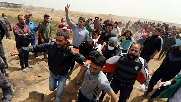 A wounded Palestinian is evacuated during clashes with Israeli troops at a protest demanding the right to return to their homeland, at the Israel-Gaza border, east of Gaza City, April 13, 2018 - Sputnik Türkiye