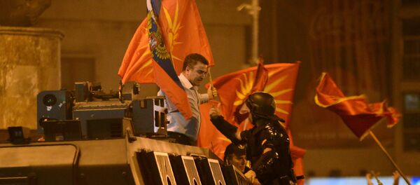 Birleşik Makedonya Partisi'nin lideri Yanko Baçev, Üsküp'te parlamento binası önünde ülkenin isminin değiştirilmesine karşı yapılan protestolarda Rusya bayrağı ve Makedonya'nın 1992-1995 yılları arasında kullandığı eski bayrağıyla zırhlı polis aracının üzerine çıktı Birleşik Makedonya Partisi'nin lideri Yanko Baçev, Üsküp'te parlamento binası önünde ülkenin isminin değiştirilmesine karşı yapılan protestolarda Rusya bayrağı ve Makedonya'nın 1992-1995 yılları arasında kullandığı eski bayrağıyla zırhlı polis aracının üzerine çıktı - Sputnik Türkiye