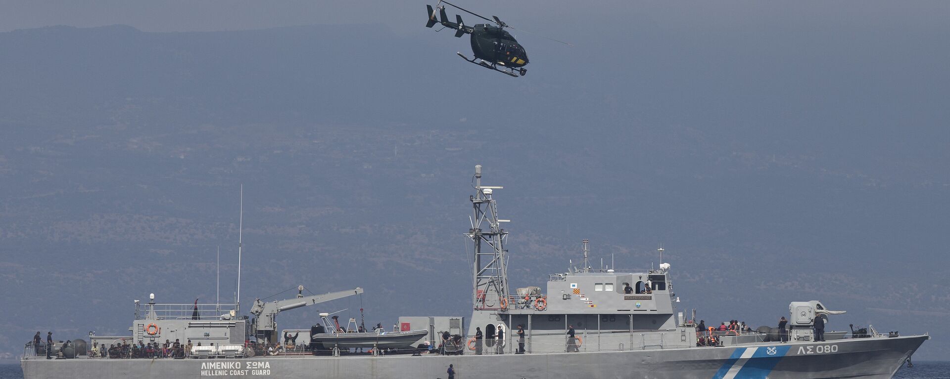 A small inflatable dinghy with a suspected smuggler on board is stopped by a Greek coastguard patrol boat, carrying migrants rescued at sea, as a helicopter from the European border control agency Frontex flies overhead, off Greece’s eastern Aegean Sea island of Lesbos on Thursday, Sept. 24, 2015 - Sputnik Türkiye, 1920, 04.05.2022