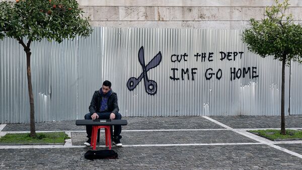 A man plays music on a digital keyboard near graffiti on a corrugated metal gate reading Cut the debt, IMF go home in Athens on February 24, 2015 - Sputnik Türkiye