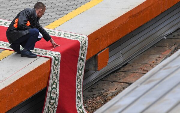 Kim'in treni perona varmadan önce kırmızı halı düzenlemelerini yapmaya çalışan bir görevli  - Sputnik Türkiye